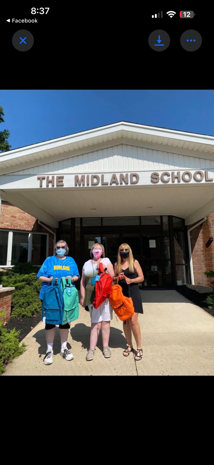 Three women outside The Midland School holding donated backpacks