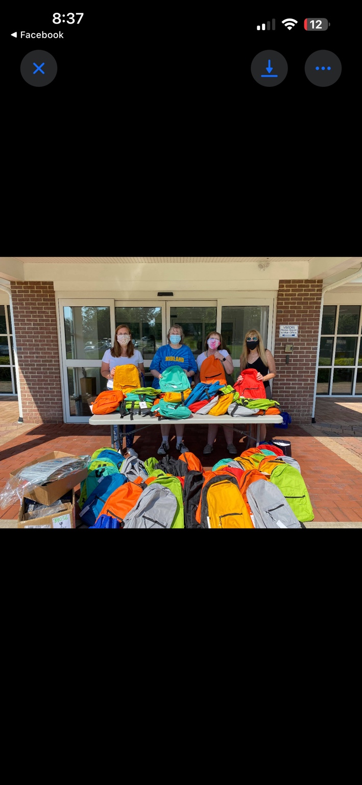 School staff and volunteers behind a table filled with brightly colored donated backpacks
